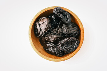 Dried prunes in wooden bowl on white background. Natural wrinkled texture of healthy sweet fruit....