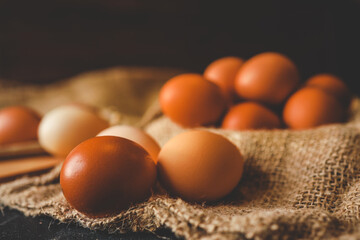 Brown farm eggs arranged in a wooden bowl and scattered on burlap fabric. Rustic dark background...