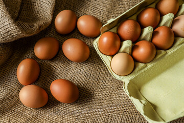 Brown organic eggs in a paper carton and scattered on rustic burlap fabric. Natural earthy tones and eco-friendly packaging emphasize farm-fresh food and sustainability