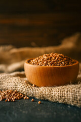 Wooden bowl filled with raw buckwheat groats on rustic burlap cloth. Healthy organic food in natural setting with warm tones and selective focus