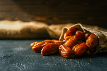 Close-up of dried dates spilling from a burlap sack onto a dark surface. The natural, sweet fruits are rich in fiber and nutrients, commonly used in healthy diets and Middle Eastern cuisine
