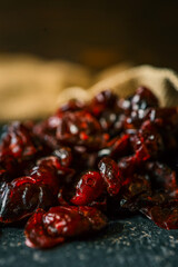 Dried cranberries spilling out of a rustic burlap sack onto a dark textured surface, perfect for...
