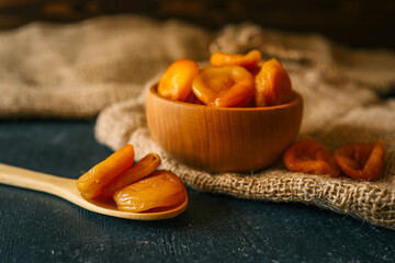 Dried apricots in a wooden bowl and spoon on rustic burlap fabric. Organic healthy snack, rich in...
