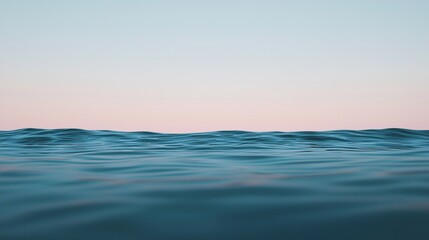 Obraz premium Calm ocean waves under a clear sky at sunset, with soft light reflecting on the water's surface.