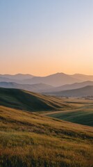 Fototapeta premium Rolling Green Grass Hills and Mountain Range at Soft Sunset Light Vertical View