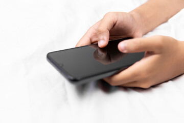 Hand holding smartphone with blank white screen on bed