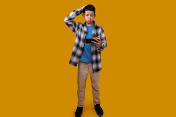Full Length of Upset Asian Child Boy Losing The Games on Mobile Phone Isolated on Yellow Background