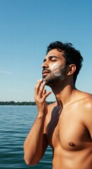 Fototapeta premium Man applying sunscreen on face outdoors for skin protection and sun care routine near lake water
