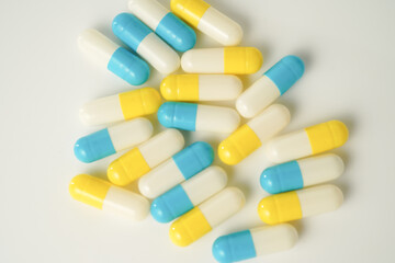 Capsules pill white blue yellow scattered on white surface, health care, medical background