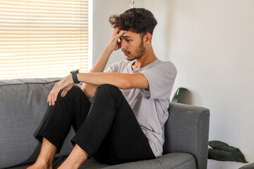 Portrait Of Depressed Young Asian Man Sitting On Sofa In Living Room At Home Alone Suffering From...
