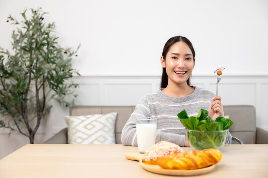 Asian woman  drinking milk and eating vegetable  breakfast  in kitchen at home .
