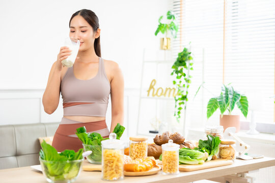 Attractive fitness asian woman finishing workout and drinking protein milk shake vitamins and vegetable after training at home. Bodybuilding. Healthy lifestyle.