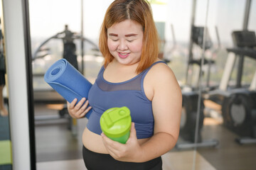 Fototapeta premium Obese asian woman in sportswear drinking protein shake from bottle After Overweight female exercising for weight loss Energy Vitality sportswoman wellness health