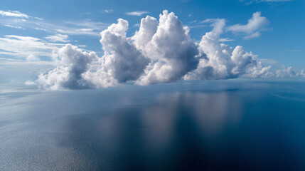 Fluffy clouds float above calm blue ocean, their reflections shimmering on water under bright sky, creating peaceful and serene atmosphere