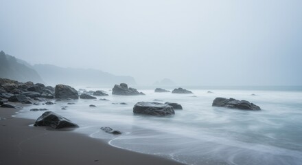 Obraz premium Misty Beach Scene with Dark Rocks and Soft Waves
