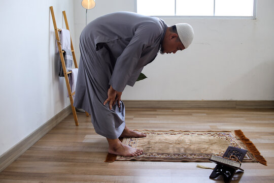Side View Of Muslim Male Praying Salah At Home Doing Ruku Movement, Kneeling