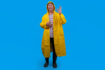 Young Asian Man in Raincoat Showing OK on Blue Background