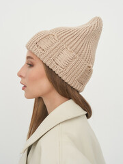 Stylish woman posing in a studio wearing a cozy knitted beanie and chic coat
