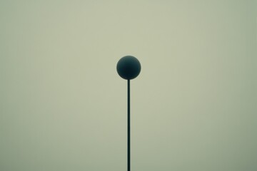 A dark sphere atop a slender pole, shrouded in a light haze