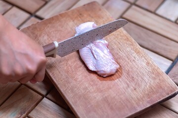 Hand holding knife to cut chicken meat on wooden chopping board