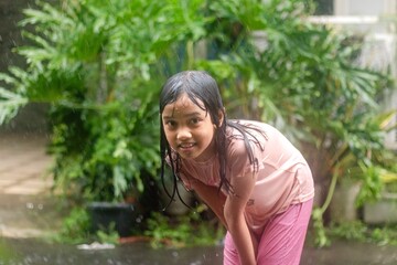 A joyful little Asian girl playing in the rain in front of the house
