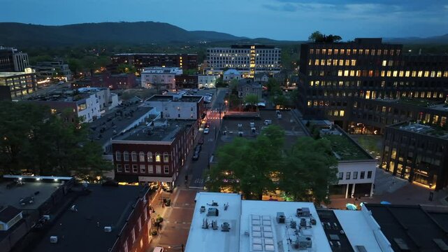 Illuminated windows and streets in Charlottesville at dusk. Aerial Orbit wide shot. Glowing office Buildings and walking people on shopping road. Virginia State, USA.