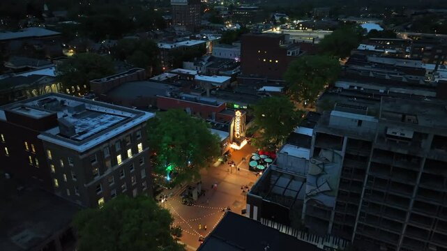 Walking people on center of american town at dusk. Aerial tilt up wide shot. Lighting Theater Building in city of Charlottesville, Virginia. Chain of lights between houses and buildings.