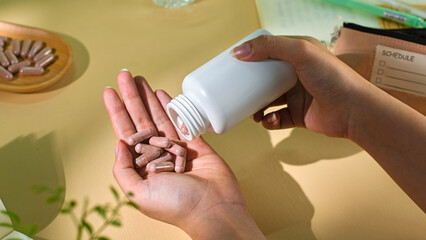 The act of pouring pills into the hand. The pills are brown capsules with white dots on the shell. Some of the pills are placed in a wooden tray. On the table are reminder to take the pills