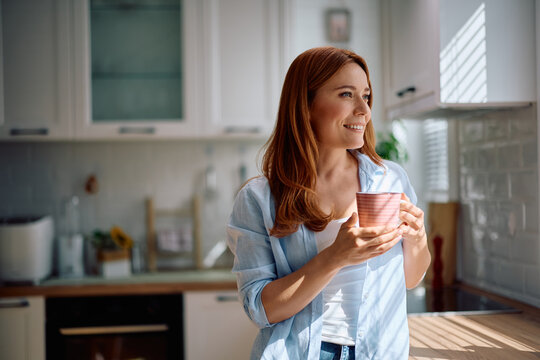 Happy woman day dreaming while having cup of tea at home.