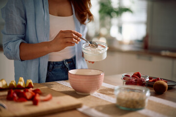 Close up of woman adding non fat yogurt while making healthy breakfast at home.