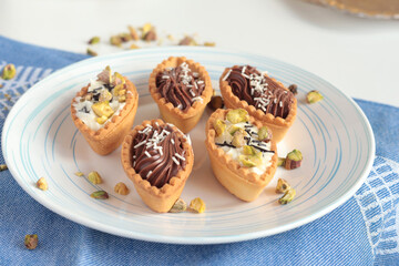 Sand dough tartlets with chocolate filling, pistachio nuts on white plate. Dessert for party, holiday. 