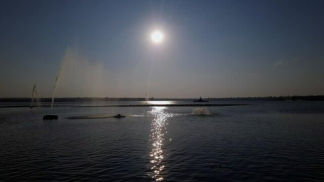 Video of water fountains or jets in a reservoir spraying water high against the shining sun at dusk