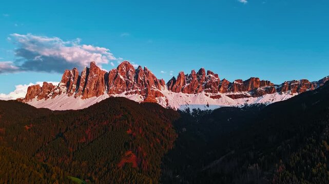 Aerial Dolomites hyperlapse. Cinema delle Odle, Geisler Peaks glowing at sunset with clouds and snowy foothills.