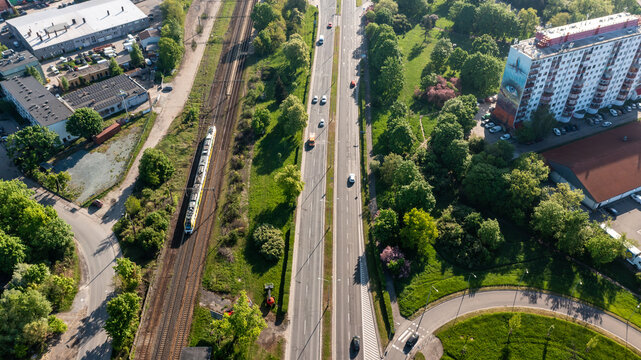 Vertical aerial view of green urban road corridor and rail line with high-rise apartments, depicting sustainable city transport and housing integration