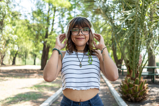 Smiling female enjoying music through headphones while relaxing outdoors on sunny day