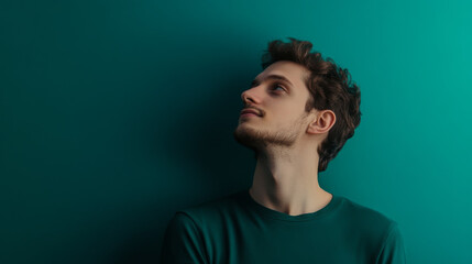 young man with curly hair is looking upwards against teal background, exuding sense of contemplation and curiosity. His expression reflects moment of introspection and wonder