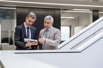 Two businessmen discussing a project using a tablet in a modern office setting