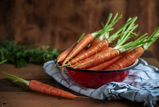 Fresh carrots in a bowl on a rustic wooden table in a studio setting