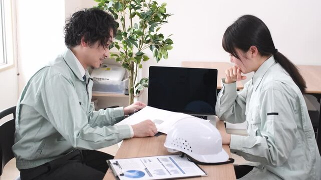 打ち合わせをする作業服を着たアジア人男女