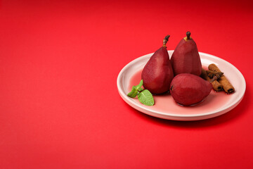 Pears in wine on plate on red background, space for text