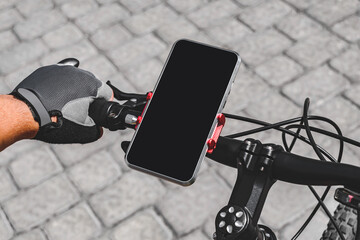 Close-up mockup of a smartphone on a bicycle handlebar. Background of gray paving tiles outdoors on...