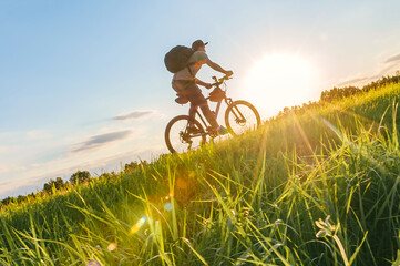 A man riding uphill on a grassy slope on a bike. Background of the sunset sun outdoors.