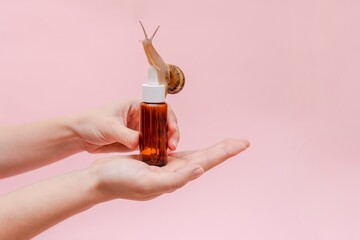 Glass cosmetic bottle with snail in hand. Mockup for your brand. Skin care product, spa, luxury,...