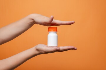 Blank bottle mockup in hand on orange background. Package for cosmetics product, nutritional supplements, vitamins, spa, beauty and luxury. Space for text