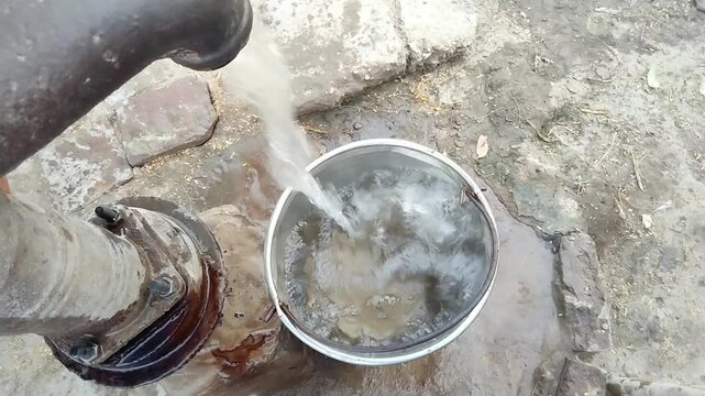 Fresh drinking water being poured from a traditional hand pump into a steel pot in a rural village &ndash; clean and natural source


