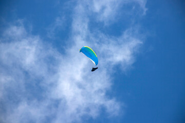 A man with a paraglider in front of a blue sky.