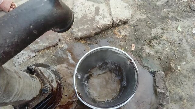 Fresh drinking water being poured from a traditional hand pump into a steel pot in a rural village &ndash; clean and natural source


