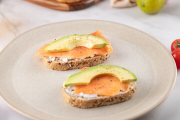 Two toasts with salmon and avocado on whole grain bread served on a beige plate. Healthy food, minimalist and natural style. Ideal for a healthy diet and conscious lifestyle