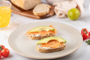 Seed bread toasts with salmon, avocado and cream cheese served on a minimalist plate. Nutritious and natural breakfast. Concept of healthy food