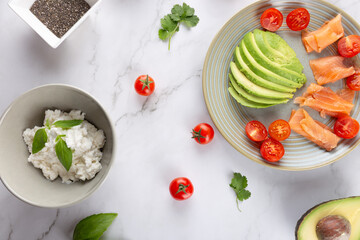 Minimalist flatlay of a healthy plate with avocado, cherry tomatoes and smoked salmon on marble background. Concept of minimalism and clean food styling
